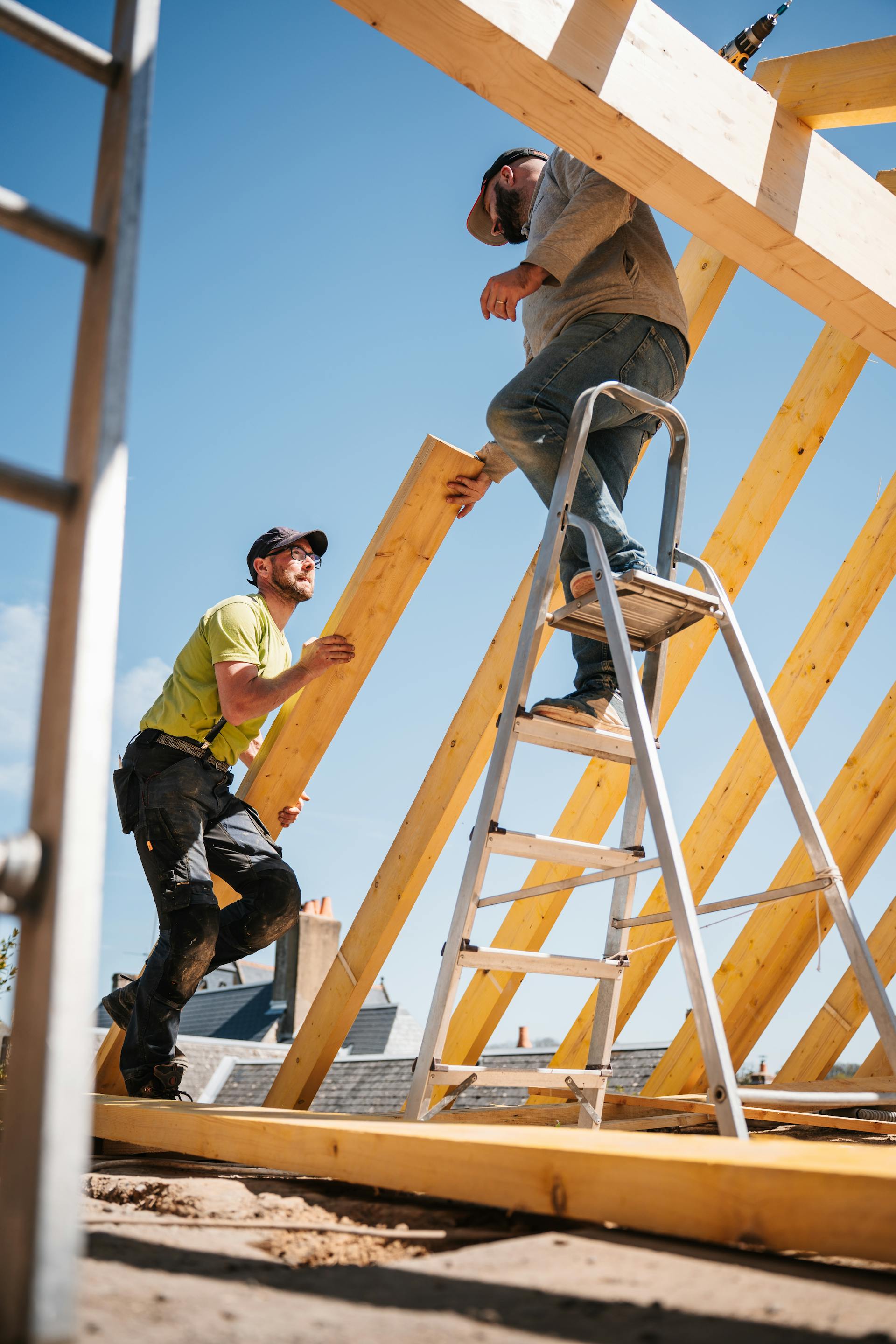 Two roofers framing a wooden roof structure on a sunny job site